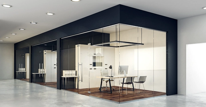 Mehrere moderne Büros mit Glaswänden und Holzböden; Schreibtische und Stühle in den Räumen; ein Computerbildschirm auf einem Schreibtisch; Deckenbeleuchtung; offene, geräumige Bürofläche rechts.