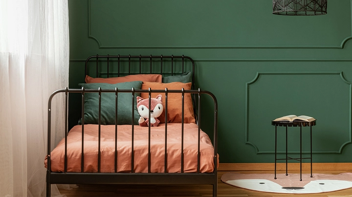 Kinderzimmer mit schwarzem Metallbett vor dunkelgüner Wand, oranger Bettbezug