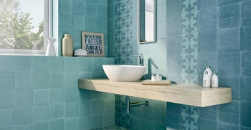 Waschbecken steht auf einem hölzernen Regalwand vor türkisfarbenen Fliesenwand in einem Badezimmer mit Dekorartikeln und einem Spiegel. Zitat im Hintergrund: NEVER RUN FASTER THAN YOUR GUARDIAN ANGEL CAN FLY.