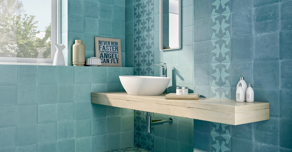 Waschbecken steht auf einem hölzernen Regalwand vor türkisfarbenen Fliesenwand in einem Badezimmer mit Dekorartikeln und einem Spiegel. Zitat im Hintergrund: NEVER RUN FASTER THAN YOUR GUARDIAN ANGEL CAN FLY.