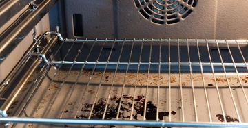 Ein Ofenrost (Objekt) mit Essensresten und Schmutz (Aktion) befindet sich in einem sauberen Ofeninnenraum (Kontext).