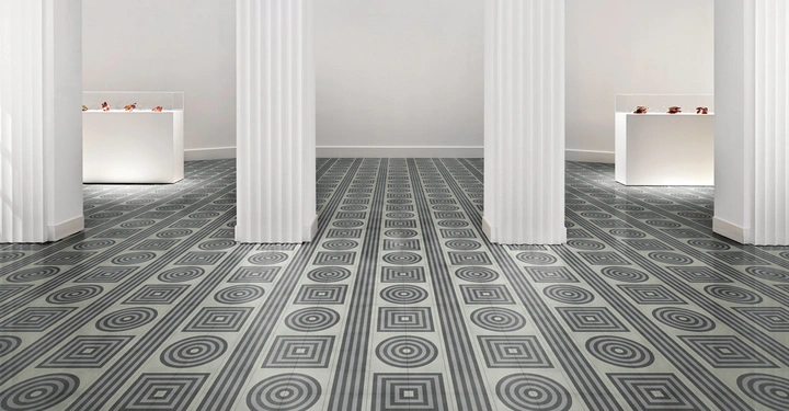 Galerie-Bild 3: Weiße Säulen stehen in einem Raum mit geometrisch gemustertem Boden Teppich. Im Hintergrund befinden sich beleuchtete Vitrinen auf weißen Sockeln, in denen kleine Gegenstände ausgestellt sind.