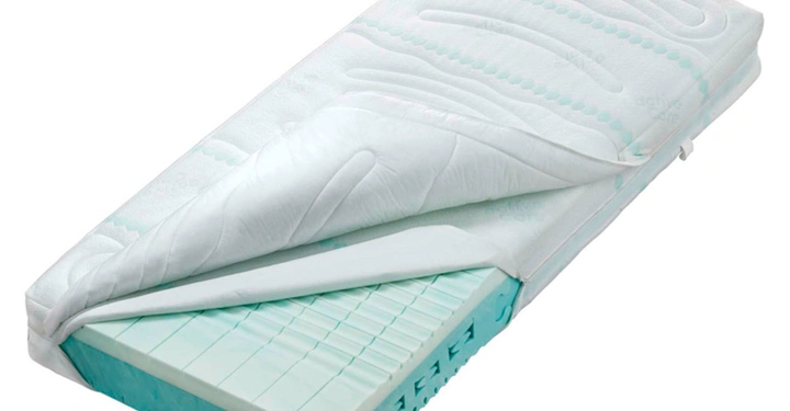 Matratze mit einer abgezogenen schützenden Hülle zeigt die blaue Schaumstoff-Polsterung darunter in einem sauberen, weißen Raum.