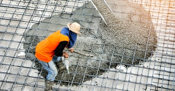 Bauarbeiter verteilt nassen Beton in eine Bewehrungsmatte auf einer Baustelle am Tag