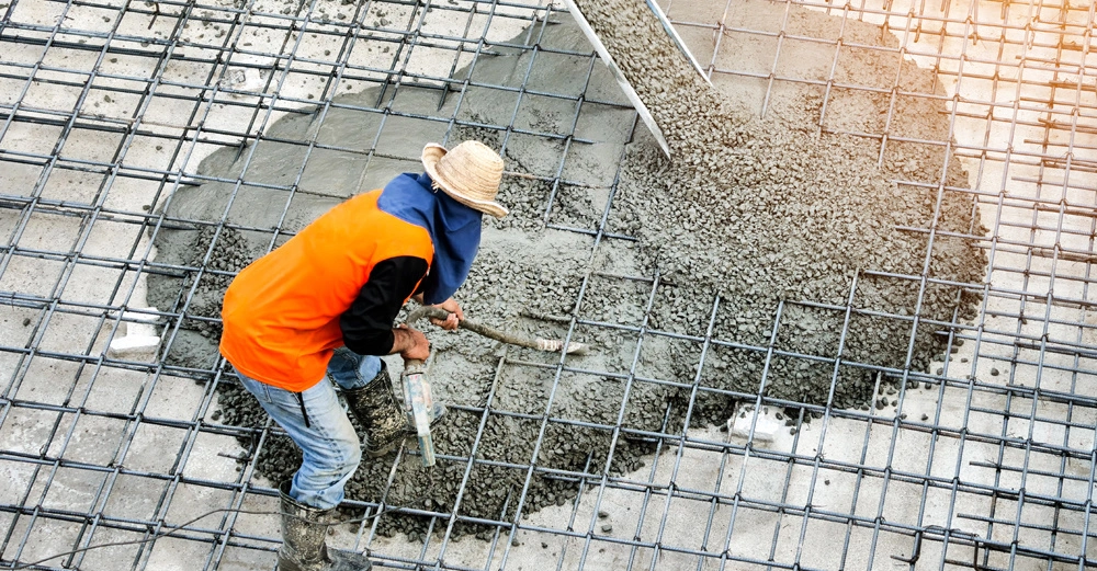 Bauarbeiter verteilt nassen Beton in eine Bewehrungsmatte auf einer Baustelle am Tag
