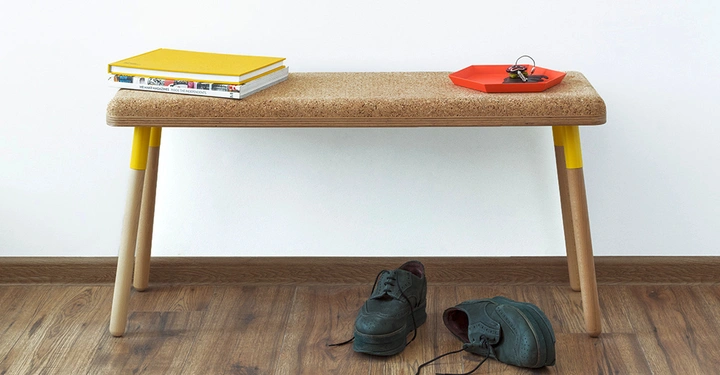 Holzbank stehend auf Holzboden hält stapelweise Bücher und ein rotes Schlüsseltablett, daneben liegen ein Paar schwarze Schuhe unordentlich auf dem Boden.