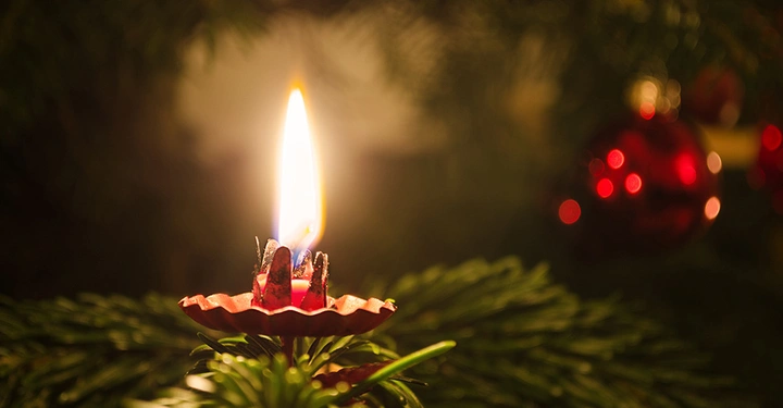 Brennende echte Wachskerze in rotem Halter am Weihnachtsbaum, ein häufiger Auslöser für Christbaumbrände.