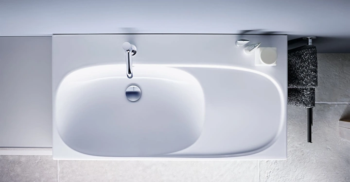 Galerie-Bild 3: Waschbecken in einem Badezimmer montiert. Wasserhahn montiert am oberen Beckenrand. Ein graues Handtuch hängt rechts. Weiße Wandfliesen und eine kleine weiße Seifenschale. Perspektive von oben.