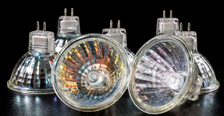 Zwei bunte Halogenstrahler liegen auf einer schwarzen Oberfläche; vier weitere Strahler stehen dahinter aufrecht und bilden einen Halbkreis.