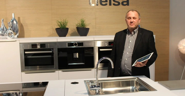 Galerie-Bild 9: Ein Mann hält ein Tablet vor einer modernen Küchenzeile mit zwei eingebauten Öfen und einer Spüle. Im Hintergrund sind zwei Pflanzen und das Schild mit der Aufschrift tielsa.