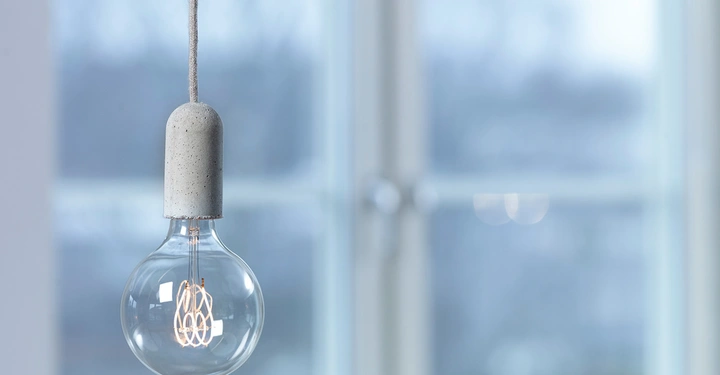 Galerie-Bild 8: Glühbirne hängt an einem Kabel leuchtet in einem modernen Interieur vor einem Fenster mit verschwommenem Hintergrund.