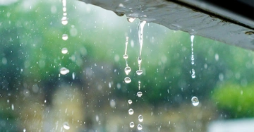 Wassertropfen fallen von einem Dach in einer regnerischen Umgebung mit verschwommenem Hintergrund aus grüner Vegetation.