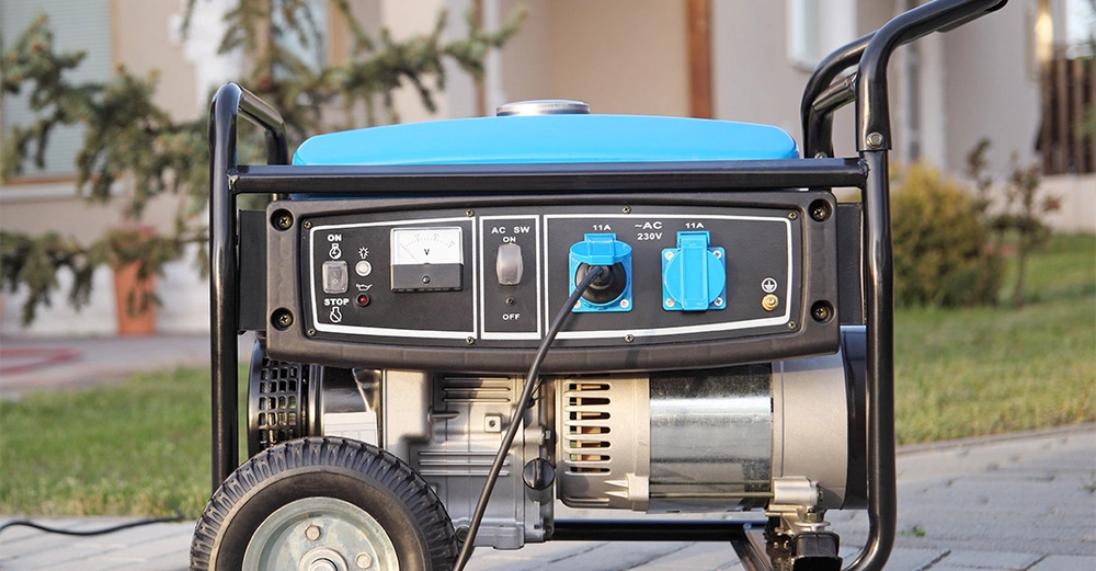 Stromgenerator steht auf einem gepflasterten Weg vor einem Haus und wird durch ein Verlängerungskabel betrieben Im Hintergrund sind Rasen und Sträucher zu sehen