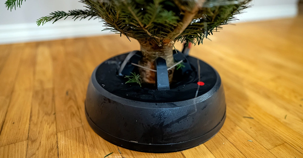 Moderner Christbaumständer mit Seilzugtechnik und Wassertank auf Parkettboden mit eingesetztem Baumstamm.