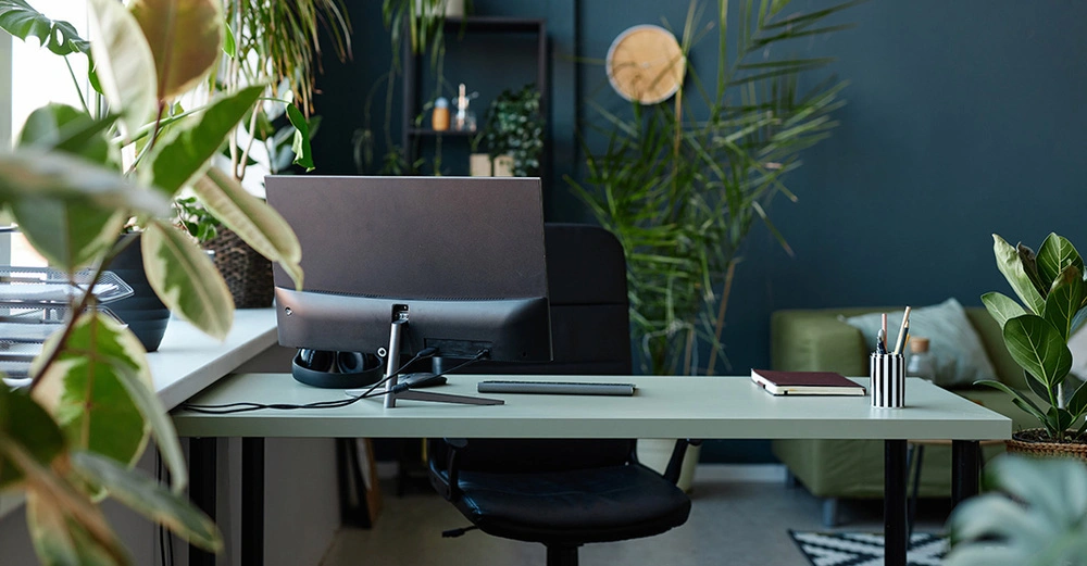 Stimmungsvolles Homeoffice mit Pflanzen, dunklen Wänden und einem Schreibtisch mit Computer.