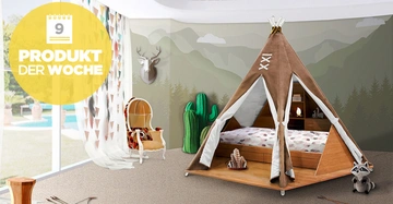 Kinderbett im Tipi-Stil mit Regalbrettern in einem verspielten Schlafzimmer mit Teppich Stapelspielzeug Sessel mit Kissen Kaktus- und Hirschdekoration Gardine mit Dreiecksmuster Großes Fenster mit Blick auf den Garten Text Inhalt: 9 PRODUKT DER WOCHE