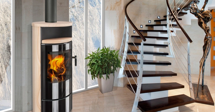 Ein Ofen brennt im modernen Wohnzimmer neben einer Treppe mit dunklen Holzstufen eine Pflanze steht daneben große Fenster zeigen verschneite Bäume draußen