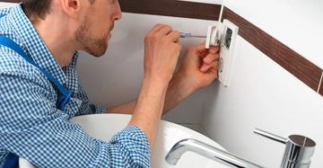 Elektriker montiert weiße Abdeckung einer Steckdose hinter Waschbecken in modernem Bad