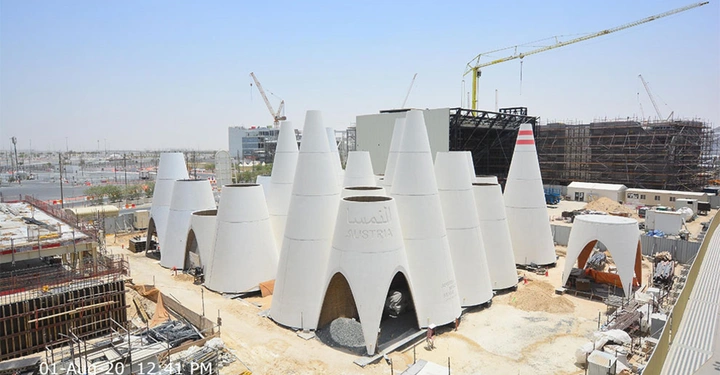 Galerie-Bild 6: Weiße Kegelförmige Gebäude stehen zusammen in einer Baustelle umgeben von Gerüsten Baukränen und Bauzäunen. Text: Austria Australie النمسا 1 AUG 20 12 41 PM