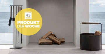 Ein Kaminbesteck steht neben einem Kamin mit Holzscheiten in einem modernen Raum mit Meerblick im Hintergrund. Gelber Kreis mit Text 45 PRODUKT DER WOCHE.