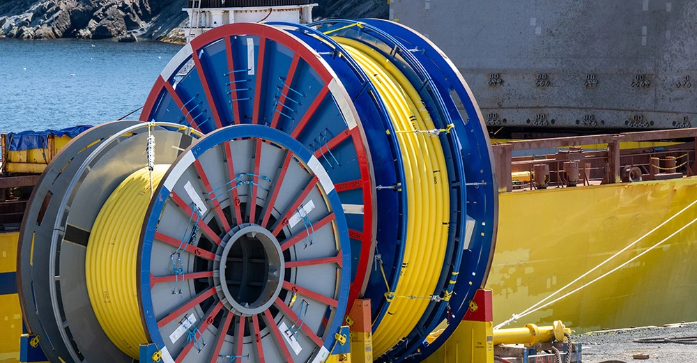 große Kabelrolle mit aufgerolltem gelbem Glasfaserkabel, fertig zum Einziehen, im Hintergrund ein graues Wohngebäude.