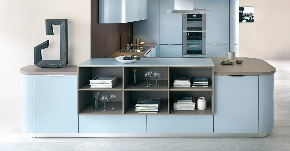 Moderne Küche mit hellblauen Schränken Steinskulptur Geschirrschrank auf Kücheninsel und integriertem Backofen Essbereich in einem lichten Raum mit einem Bild an der Wand.