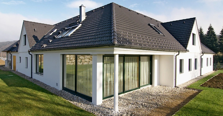 Galerie-Bild 1: Weißes Einfamilienhaus mit schwarzem Dach und großen Fenstern auf einem gepflegten Rasen mit Kieselsteinen umgeben in einer ländlichen Umgebung mit Bäumen im Hintergrund