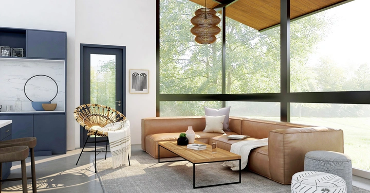 Ledersofa steht vor großen Fenstern im modernen Wohnzimmer daneben ein kleiner Holztisch mit Dekorationen ergänzt von Stuhl und Hocker im Hintergrund Küche mit blauer Wand und hängender Lampe