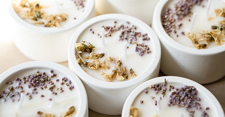 5 selbst gemachte Duftkerzen in weißen Betonbehältern, dekoriert mit frischem Lavendel und Blütenblättern.