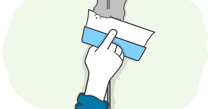 Hand trägt mit einer Spachtel graue Verputzmasse auf eine Wand auf in einem pastellgrünen Hintergrund.