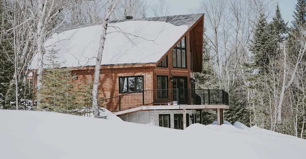 Modernes Blockhaus mit großer Fensterfront am Rand eines verschneiten Waldes