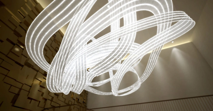 Leuchtende, gewundene Lichtbänder hängen von der Decke in einem modernen, abstrakten Raum mit strukturierten Wänden.