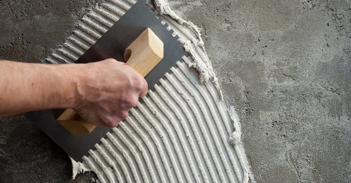 Hand hält Kelle streicht Kleber glatt Betonhintergrund