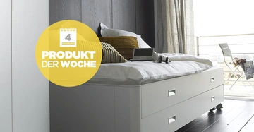 Ein weißes Bett mit Schubladen darauf liegen ein Laptop Kopfhörer und Kissen es steht in einem modernen Schlafzimmer mit Holzboden und Fenster. Text: 4 PRODUKT DER WOCHE.