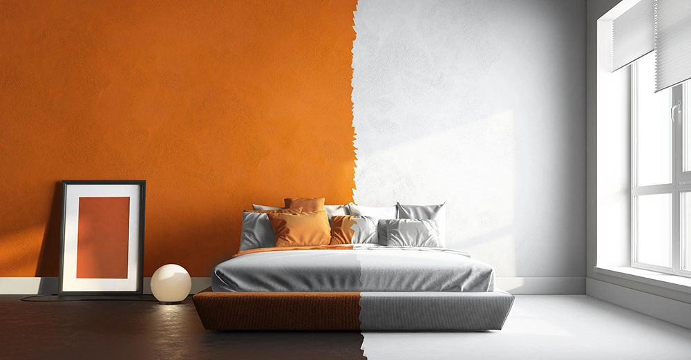 Bett steht in einem halb orange halb weiß gestrichenen Zimmer rechts Fenster beleuchtet den Raum links ist ein gerahmtes Bild an die Wand gelehnt neben einer kugelförmigen Lampe