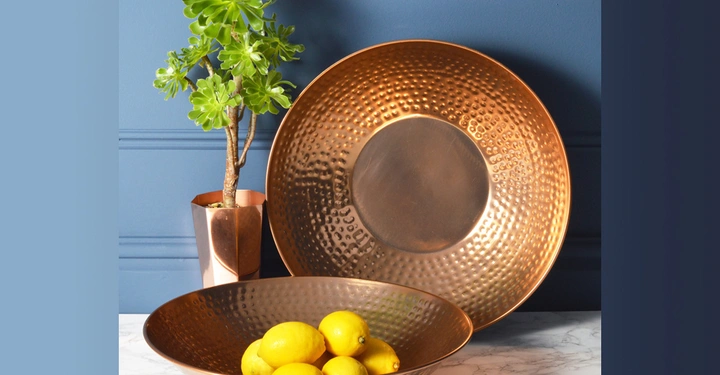 Galerie-Bild 7: Kupferschale enthält Zitronen auf weißer Marmoroberfläche Kleine Pflanze in Kupfertopf steht daneben Hintergrund ist eine blau gestrichene Wand