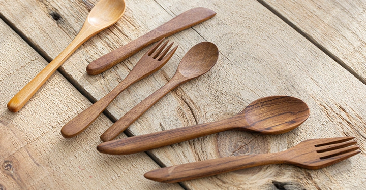 Holzdielen auf denen ein heller Holzlöffel und mehrere Löffel und Gabeln aus dunklem Olivenholz liegen. Essbesteck aus Holz