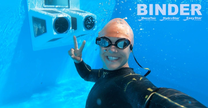 Galerie-Bild 3: Mensch im Taucheranzug und Schwimmbrille macht ein Victory-Zeichen unter Wasser vor einem technischen Gerät in einem Pool. Text: BINDER MecaTec HydroStar EasyStar.