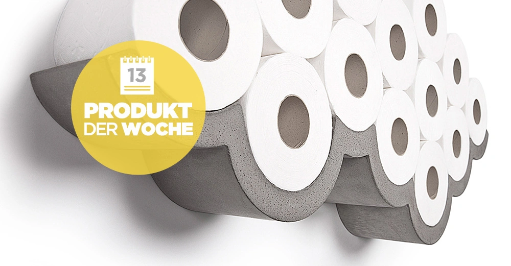 Ein wandmontiertes Regal hält mehrere Rollen Toilettenpapier zusammen in Form einer Wolke. Gelber runder Aufkleber mit Text: 13 Produkt der Woche.