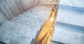 Betontreppe führt nach unten Baustelle Holzgeländer umgeben von Baugerüsten und Werkzeugen Baustrahler liefern Beleuchtung Wände aus Beton Rohbauumgebung