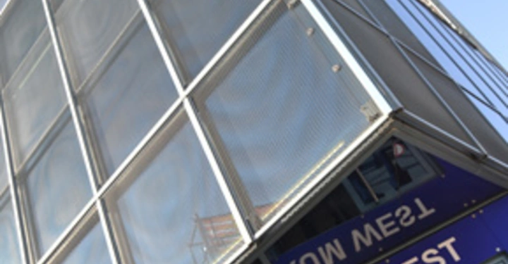 Galerie-Bild 11: Hoches Gebäude mit Glasfassade steht neben Eingang mit Text MESSEZENTRUM WEST Situation in urbaner Umgebung bei klarem Himmel.