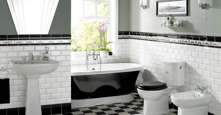 Galerie-Bild 5: Keramikwaschbecken an der Wand mit Spiegel und schwarzem Handtuch rechts daneben freistehende Badewanne Badezimmerfliesen in schwarz-weißem Karomuster hellem Tageslicht das durch Fenster strömt hinten Toilette und Bidet.