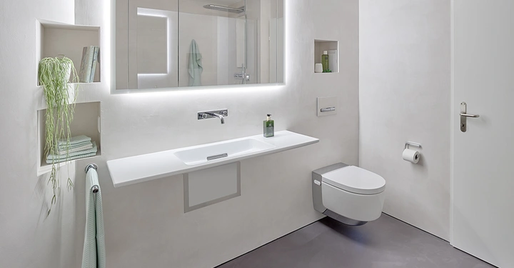 Galerie-Bild 1: Ein weißes Badezimmer mit schwebendem Waschbecken und wandhängender Toilette in einer modernen, minimalistischen Umgebung. Handtuchhalter, Regale mit Pflanzen und Pflegeprodukten links und rechts vorhanden.