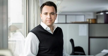 Ein Mann steht an einem Fenster und schaut in die Kamera Büro im Hintergrund mit Schreibtischen und Stühlen Büroflur.