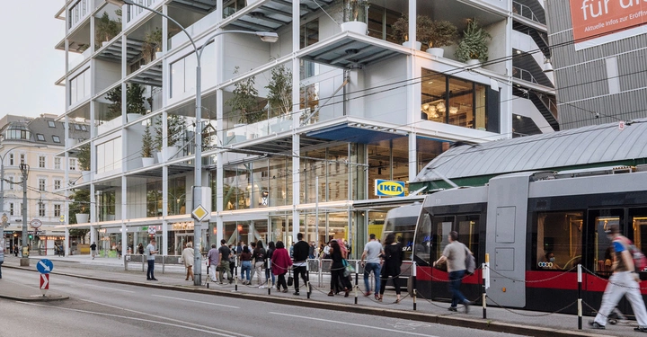 Galerie-Bild 3: Menschen gehen auf dem Gehweg neben einer Straßenbahn vor einem mehrstöckigen Gebäude mit Glasfassade und Pflanzen. Ein IKEA-Schild ist sichtbar auf dem Gebäude.
