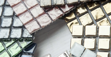 Mehrere Stapel bunter Glasfliesen liegen auf einer weißen Oberfläche. Die Fliesen sind quadratisch und in unterschiedlichen Farben wie Grün, Gold und Rosa gestaltet.