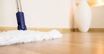 Wischmopp reinigt Laminatboden moderne Wohnung mit weißer Vase im Hintergrund.