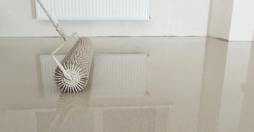 Eine Stachelwalze glättet eine nasse Oberfläche in einem hellen Raum neben einem Heizkörper an der Wand.