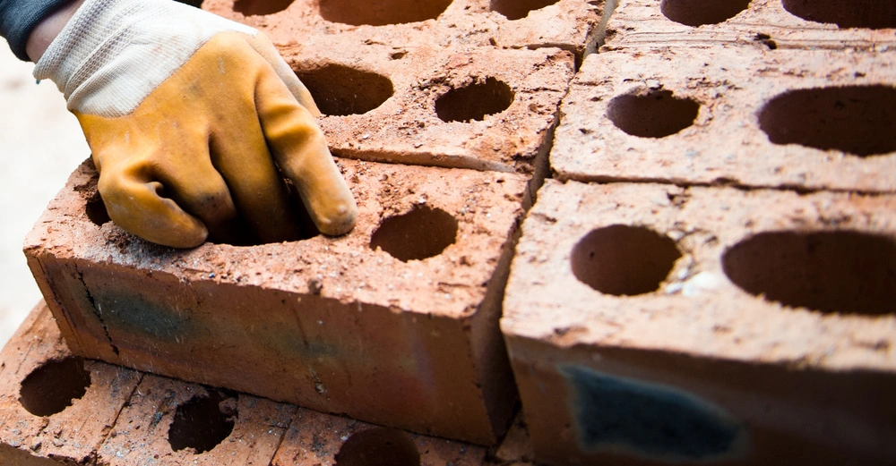 Handschuhtragende Hand greift in einen Hohlziegel inmitten mehrerer gestapelter Hohlziegel bei Tageslicht