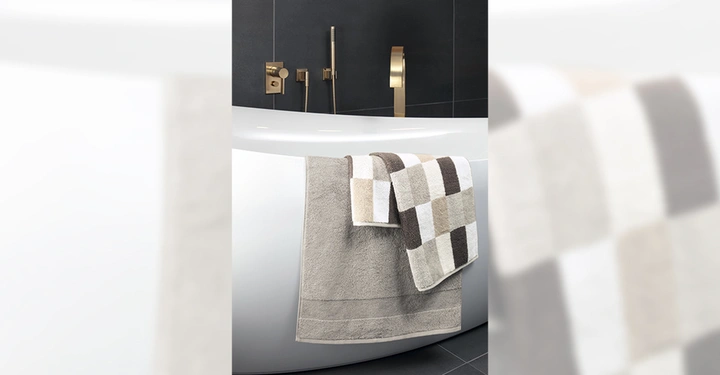 Badewanne mit zwei Handtüchern Beige Handtuch und kariertes Handtuch dekoriert Dunkles Badezimmer mit modernen goldenen Armaturen und dunklen Fliesen